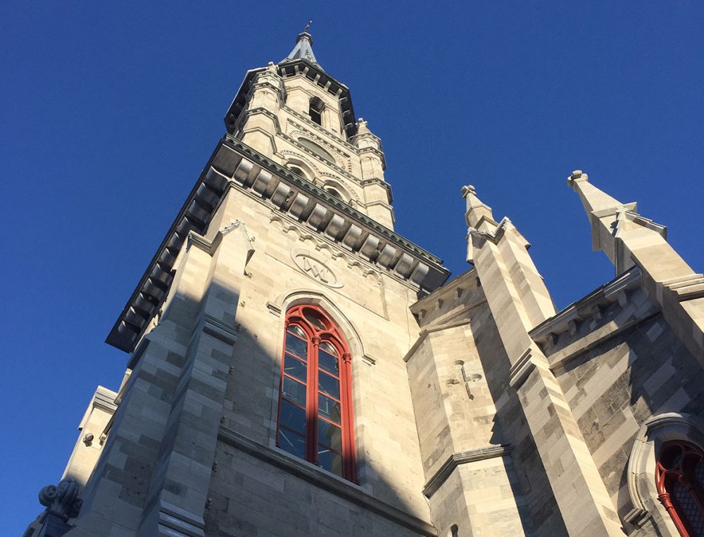 Looking up at a stone clock tower against a blue sky.